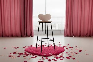 STOOL SHOWING A Pink heart shaped rug on the floor and a light pink pillow on the stool.   